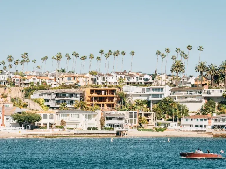 Waterfront houses with palm trees behind and a small boat on the water in the foreground.