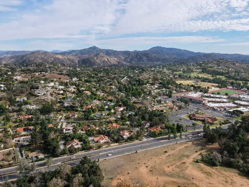 Suburban neighborhood with houses, roads, and mountains in the background under a partly cloudy sky.