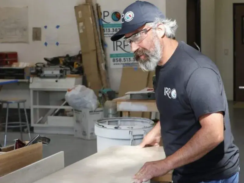 Man wearing safety glasses and a cap working with a large piece of wood in a workshop.