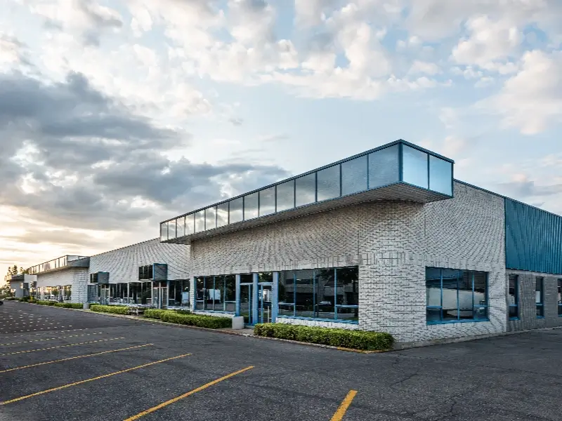 Modern commercial building with large windows and an empty parking lot under a cloudy sky.