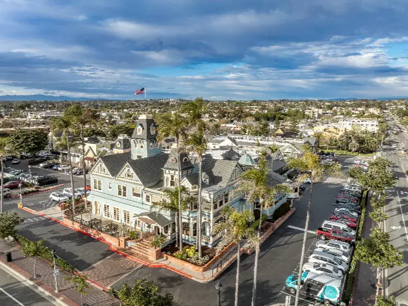 Large Victorian-style building surrounded by palm trees and parking lots under a cloudy sky.
