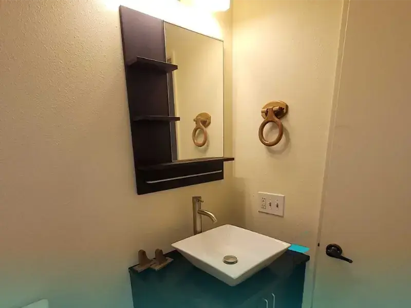 Bathroom sink with a square basin, wall-mounted mirror with shelves, and a wooden towel ring.