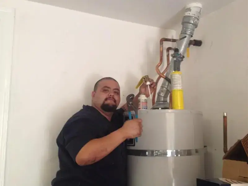 A man holding a wrench working on a water heater with pipes.